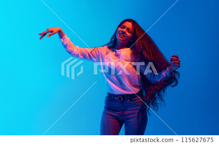 Young woman, attractive Indian person dancing and singing in neon light against blue gradient background. 115627675