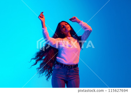 Young sensual, joyful Indian woman dress casual attire moves in dance against green studio background. in neon light against blue gradient background. 115627694