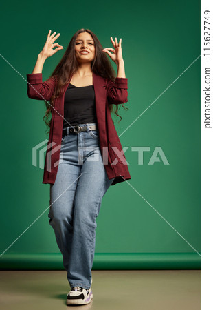 Happy young Indian woman dressed casual attire dancing and gesturing against green studio background. Happy young Indian woman dressed casual attire dancing and gesturing against green studio background. 115627749