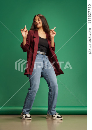 Overjoyed young Indian woman dressed casual attire dancing and gesturing against green studio background. Overjoyed young Indian woman dressed casual attire dancing and gesturing against green studio background. 115627750