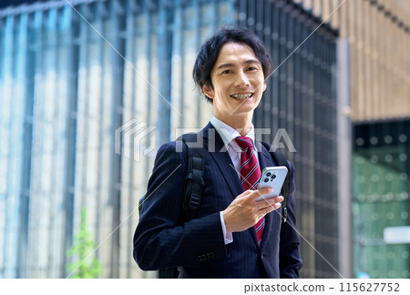 穿著西裝背著背包操作智慧型手機的商人 穿著西裝背著背包操作智慧型手機的商人 115627752