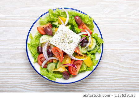 Traditional Greek Salad with Feta Cheese, Tomatoes, Bell Pepper, Cucumbers, Olives, Herbs in white ceramic bowl on White rustic wooden table background top view, Cuisine of Greece Traditional Greek Salad with Feta Cheese, Tomatoes, Bell Pepper, Cucumbers, Olives, Herbs in white ceramic bowl on White rustic wooden table background top view, Cuisine of Greece 115629185