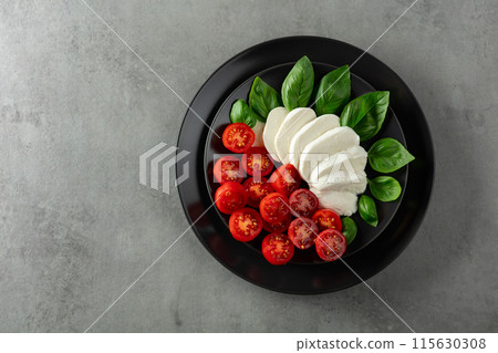 Mozzarella with basil and cherry tomatoes on a black plate. 115630308
