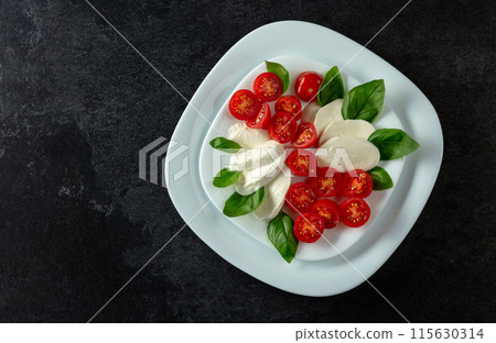 Mozzarella with basil and cherry tomatoes on a black background. Mozzarella with basil and cherry tomatoes on a black background. 115630314