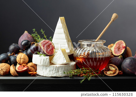 Camembert cheese with fruits and honey on a black background. 115630328