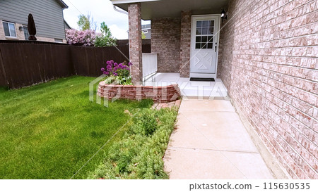 The front porch of a charming brick house featuring a white door and a well-maintained garden bed with blooming purple flowers. The neatly trimmed lawn and inviting entryway enhance the home curb 115630535
