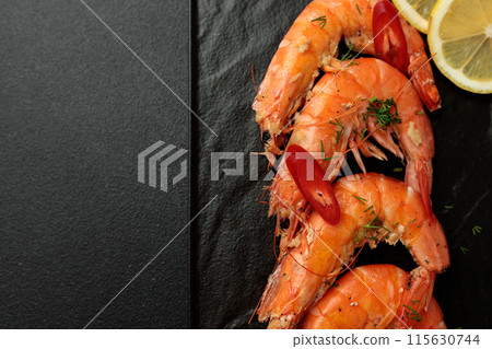 Large cooked king prawns on a black background. Lemon slices Large cooked king prawns on a black background. Lemon slices 115630744