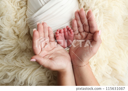 Feet of the newborn on the palms of the parents. The palms of the father and mother are holding the foot of the newborn baby in a white flokati blanket. Photography of a child's toes, heels and feet.  115631087