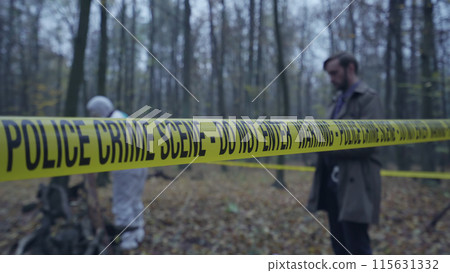 Police detective and forensics team conduct their investigation behind crime scene tape Police detective and forensics team conduct their investigation behind crime scene tape 115631332
