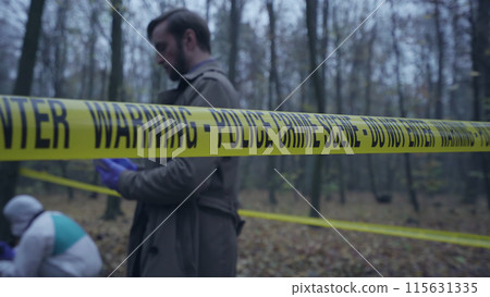 View of forensics experts and a detective working behind crime scene tape during an investigation View of forensics experts and a detective working behind crime scene tape during an investigation 115631335