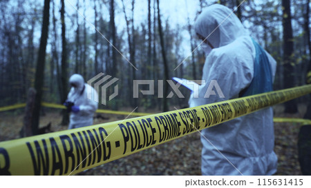 Forensic analysts work at a crime scene secured by tape, focusing on evidence collection Forensic analysts work at a crime scene secured by tape, focusing on evidence collection 115631415
