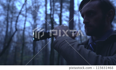 Brave detective searches for a cruel murderer in a rainy forest, holding a flashlight Brave detective searches for a cruel murderer in a rainy forest, holding a flashlight 115631468
