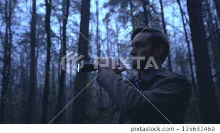 Detective looks for evidence in a rainy forest with a flashlight in hand, conducting an investigation Detective looks for evidence in a rainy forest with a flashlight in hand, conducting an investigation 115631469
