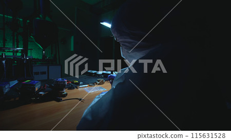 Engineer solders in a lab at night, crafting an improvised bomb in a hazardous experiment 115631528