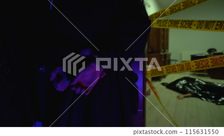 Policeman handcuffs the murderer, with a dead body lying on the floor, at the scene of a bloody crime 115631550