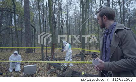 Busy policeman writing in a notepad, forensic investigators examining a crime scene 115631566