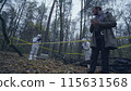 Police detective taking notes at a forest crime scene marked with yellow tape 115631568
