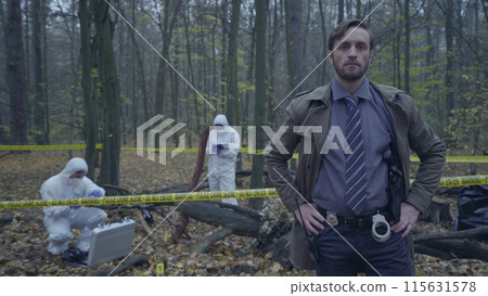 Concerned police detective looking at the camera, experts working at a crime scene Concerned police detective looking at the camera, experts working at a crime scene 115631578