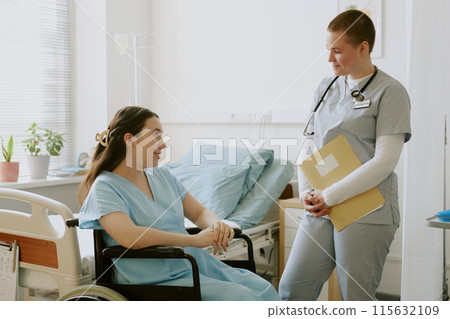 Young nurse holding yellow folder and listening to young woman in labor while she sitting in wheelchair Young nurse holding yellow folder and listening to young woman in labor while she sitting in wheelchair 115632109