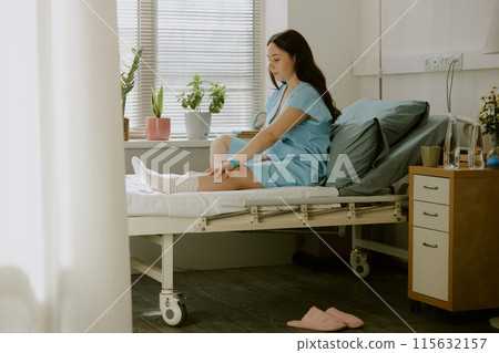 Pregnant woman sitting on bed and stretching her leg while she preparing for labor Pregnant woman sitting on bed and stretching her leg while she preparing for labor 115632157