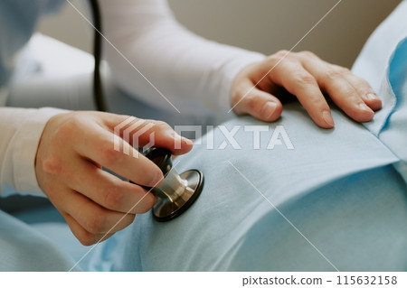 Medium close up of doctors hand holding stethoscope and touching pregnant belly while she listening to unborn babys heartbeat Medium close up of doctors hand holding stethoscope and touching pregnant belly while she listening to unborn babys heartbeat 115632158