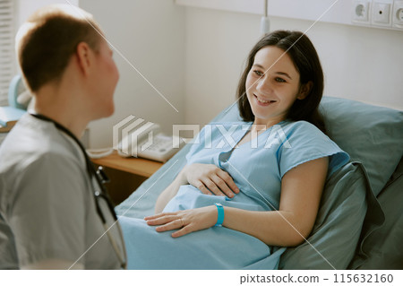 Pregnant woman lying on hospital bed and looking at nurse with wide smile 115632160