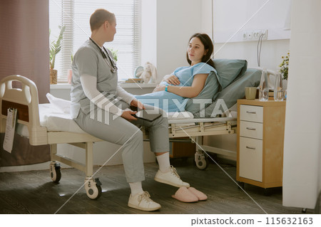 Obstetrician visiting young pregnant woman and having discussion with her in hospital ward Obstetrician visiting young pregnant woman and having discussion with her in hospital ward 115632163