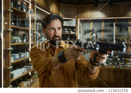 Portrait of mature male in shop merchant with two handguns aiming Portrait of mature male in shop merchant with two handguns aiming 115632250