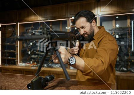 Closeup of male customer testing new model of automatic rifle in weapon store 115632260