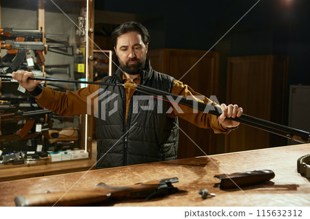 Seller cleaning gun with ramrod while working in hunting shop 115632312