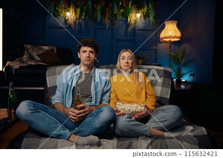 Sad couple watching emotional film with popcorn together 115632421