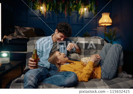 A couple sit on a comfortable couch enjoy popcorn and beer 115632425