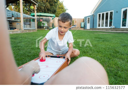 Joyful little boy playing portable air hockey with his mom in the garden. Fun Playing Games in Backyard Lawn on Summer Day. Happy family time together. Solo parenting. Active childhood 115632577