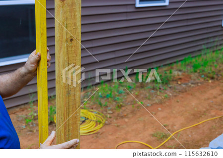 Building wooden fence in backyard checking posts with level 115632610