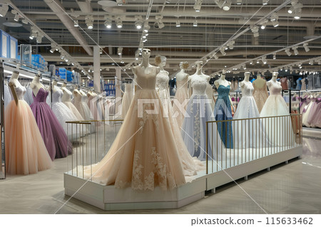 The large space of the shopping mall is decorated with an elegant display stand displaying wedding dresses in various colors and designs, including white gowns, light blue and purple tulle dresses, pi 115633462