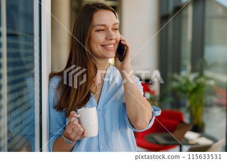 A woman is happy talking on her phone and drinking from a mug in a modern office A woman is happy talking on her phone and drinking from a mug in a modern office 115633531