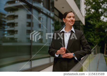 A businesswoman is posing outdoors with a tablet in front of an office building A businesswoman is posing outdoors with a tablet in front of an office building 115633589