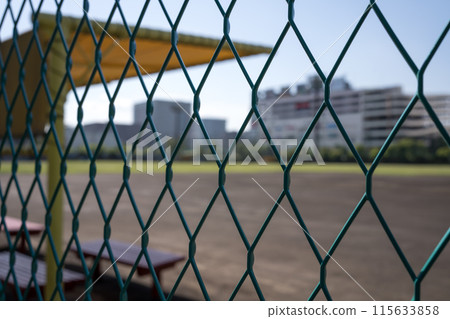A dirt baseball field seen through the fence on a sunny day A dirt baseball field seen through the fence on a sunny day 115633858