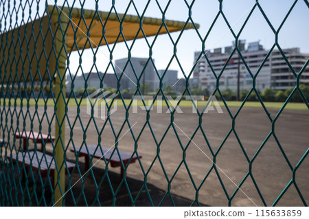 A dirt baseball field seen through the fence on a sunny day A dirt baseball field seen through the fence on a sunny day 115633859