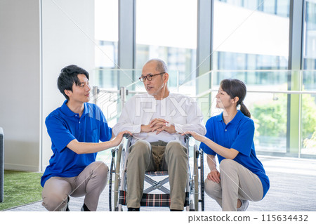 Senior man in a wheelchair and male and female staff at a care facility 115634432