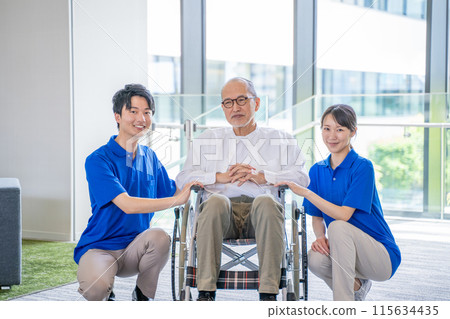 Senior man in a wheelchair and male and female staff at a care facility Senior man in a wheelchair and male and female staff at a care facility 115634435