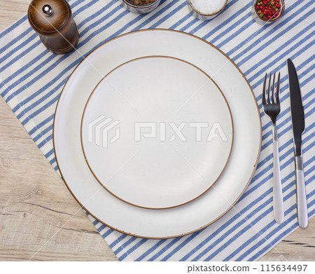 Round empty white ceramic plate, knife and fork on the table, top view 115634497