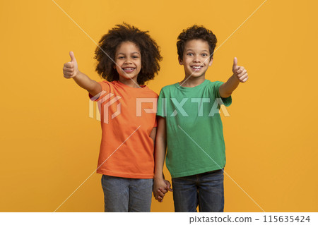 Two African American kids, one boy and one girl, are smiling and giving thumbs up gestures, bright yellow background. They appear cheerful and enthusiastic, showing approval in an expressive way. Two African American kids, one boy and one girl, are smiling and giving thumbs up gestures, bright yellow background. They appear cheerful and enthusiastic, showing approval in an expressive way. 115635424