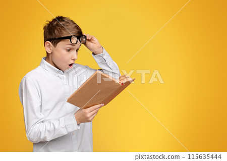 A young boy wearing glasses engrossed in reading a book. 115635444