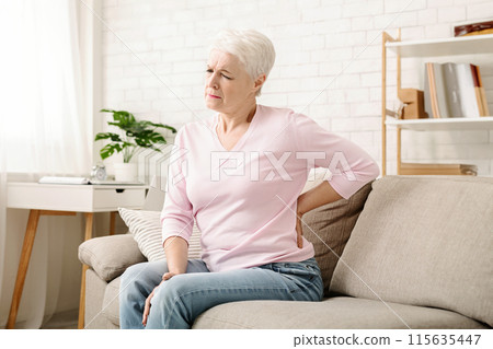 Senior woman suffering from backache, sitting on couch and touching loin at home, empty space Senior woman suffering from backache, sitting on couch and touching loin at home, empty space 115635447