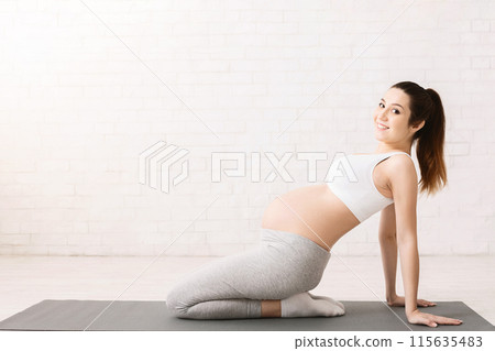A pregnant woman is engaged in a yoga pose, showcasing flexibility and balance while maintaining physical wellness during pregnancy, copy space 115635483