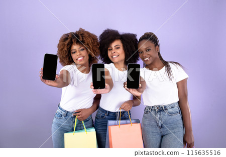 Shopping App Concept. Smiling Black Women Trio Showing Phones Blank Screens Advertising Application, Holding Shopper Bags With Purchases On Purple Studio Background. Mockup 115635516
