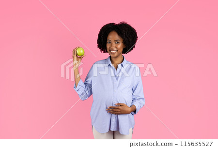 Glad millennial black lady vegan with big belly hold green apple, enjoy fruit, isolated on pink background, studio. Recommendation vitamins, proper nutrition, health care and diet Glad millennial black lady vegan with big belly hold green apple, enjoy fruit, isolated on pink background, studio. Recommendation vitamins, proper nutrition, health care and diet 115635527