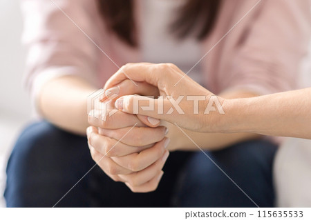 Two individuals sit closely, offering solace through hand-holding. Their intertwined hands signify support and empathy, creating a comforting atmosphere indoors, cropped 115635533