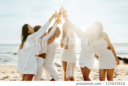 Group of ladies drinking champagne while having a hen party on the beach, women hanging out, celebrating bachelorette party on coastline at sunset Group of ladies drinking champagne while having a hen party on the beach, women hanging out, celebrating bachelorette party on coastline at sunset 115635618